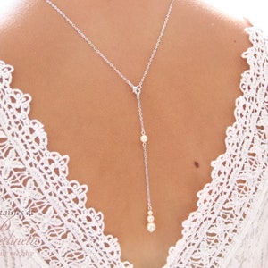 May include: A silver chain necklace with a pearl pendant. The necklace is worn by a person with a white lace top.