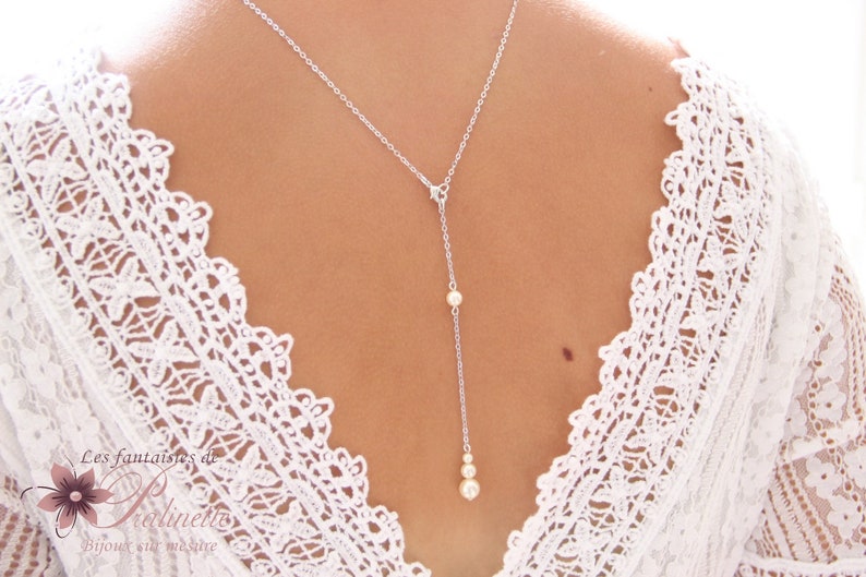 May include: A silver chain necklace with a pearl pendant. The necklace is worn by a person with a white lace top.