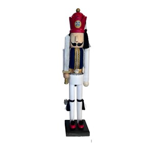 May include: A wooden nutcracker figurine of a soldier wearing a red hat with a gold crown, a blue and gold uniform, and white pants. He is holding a sword in his right hand and has a black tassel hanging from his hat.