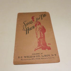 May include: Vintage songbook titled "Songs for the Hour" featuring a red illustration of the Statue of Liberty. Published by S.C. Wells & Co. Le Roy, N.Y. The cover is a faded tan color.