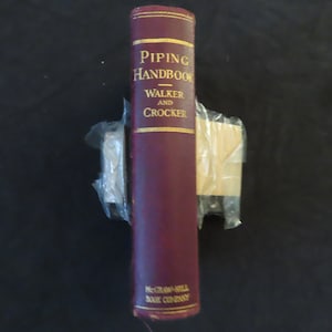 May include: A maroon-colored "Piping Handbook" book by Walker and Crocker, with gold lettering and trim. The book is wrapped in clear plastic and tape. The McGraw-Hill Book Company logo is at the bottom.