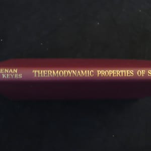 May include: A maroon book titled "Thermodynamic Properties of Steam" by Keenan and Keyes. The text is in gold lettering. The book is lying on a dark surface.
