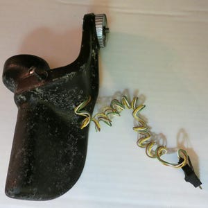 May include: A black, curved mechanical component with a silver gear and a coiled wire with yellow and green insulation. The component has a textured surface and is set against a white background.