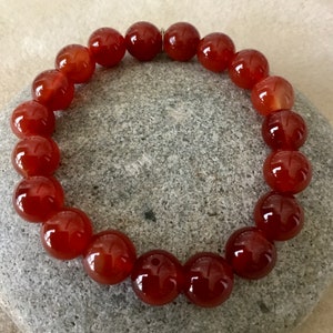 May include: A red carnelian gemstone bracelet with round beads. The bracelet is made of natural stones and is approximately 7 inches in length.