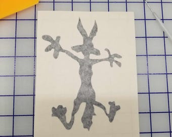 May include: A gray vinyl decal of a cartoon coyote with its arms outstretched and legs bent, as if running. The decal is on a white background.