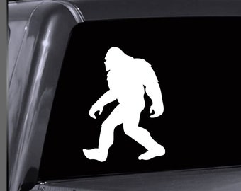 May include: White silhouette of Bigfoot walking on a black background. The silhouette is a vinyl decal sticker.