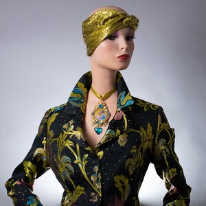May include: A mannequin wearing a black and gold patterned jacket with a gold turban and a gold necklace with a blue and gold pendant.