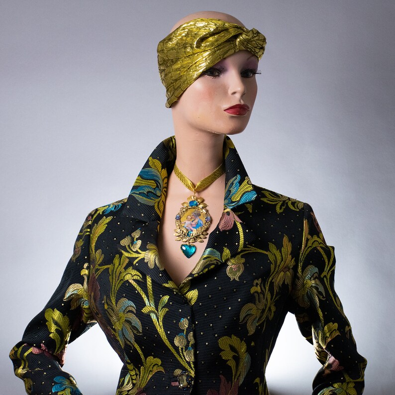 May include: A mannequin wearing a black and gold patterned jacket with a gold turban and a gold necklace with a blue and gold pendant.