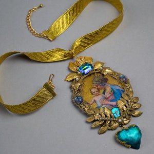 May include: Gold necklace with a large pendant featuring a religious image of the Virgin Mary holding a baby Jesus. The pendant is decorated with gold leaves, pearls, and blue and green gemstones. The necklace is made of a gold ribbon.