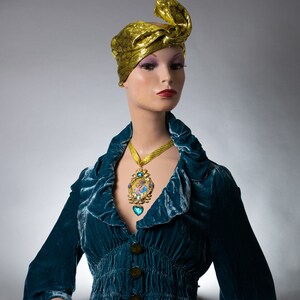 May include: A mannequin wearing a teal blue velvet dress with a gold and blue pendant necklace and a gold turban.