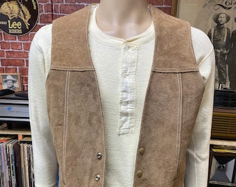 May include: A brown suede vest with a white undershirt and blue jeans. The vest has a snap closure and a pointed collar.