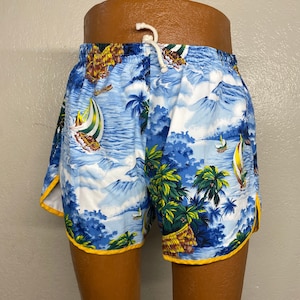 May include: Blue and white shorts with a tropical print featuring sailboats, palm trees, and mountains. The shorts have a yellow trim and a white drawstring. The fabric has a Hawaiian theme.