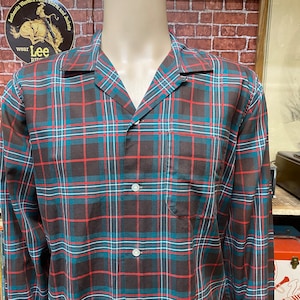 May include: A long-sleeved button-down shirt with a brown, red, and blue plaid pattern. The shirt has a collar and a pocket on the left side.