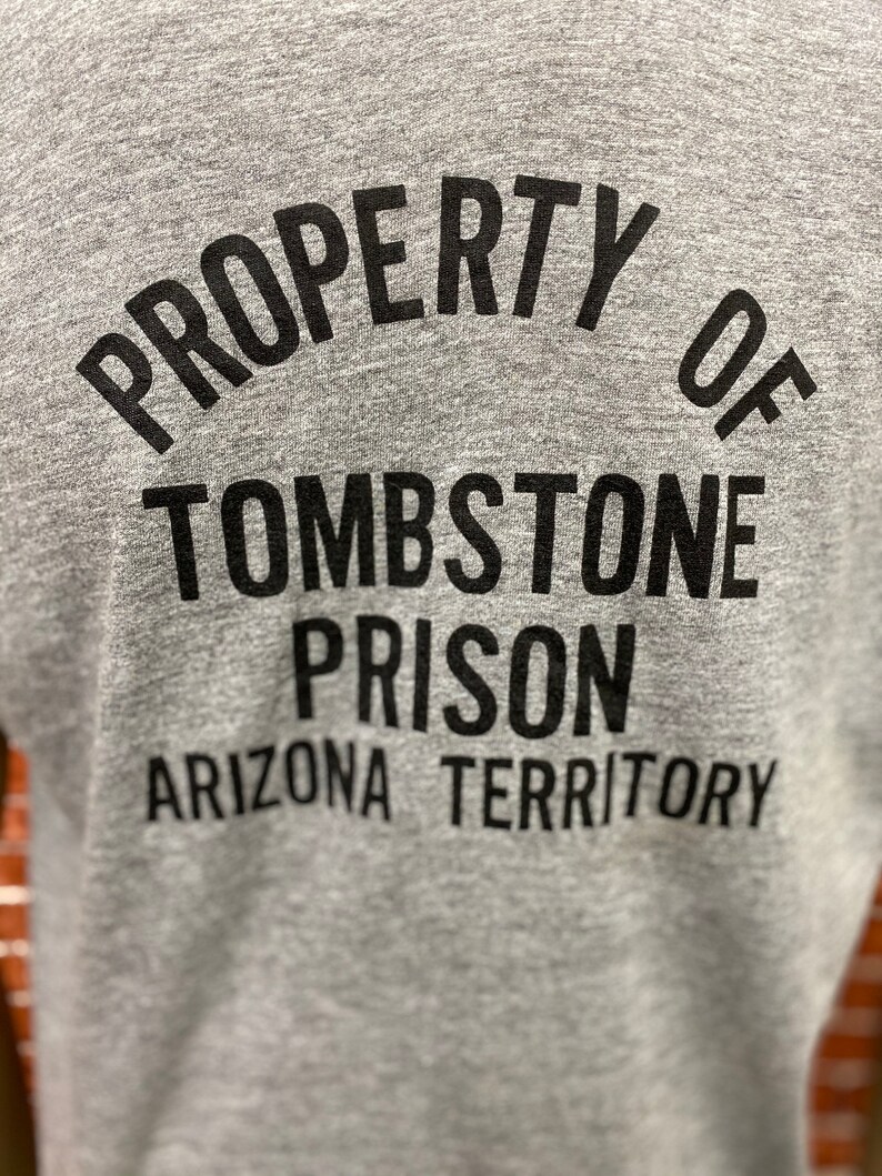May include: Gray t-shirt with black text that reads "PROPERTY OF TOMBSTONE PRISON ARIZONA TERRITORY".