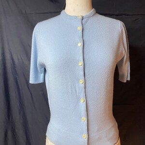May include: A light blue short-sleeved cardigan with a button-up front.