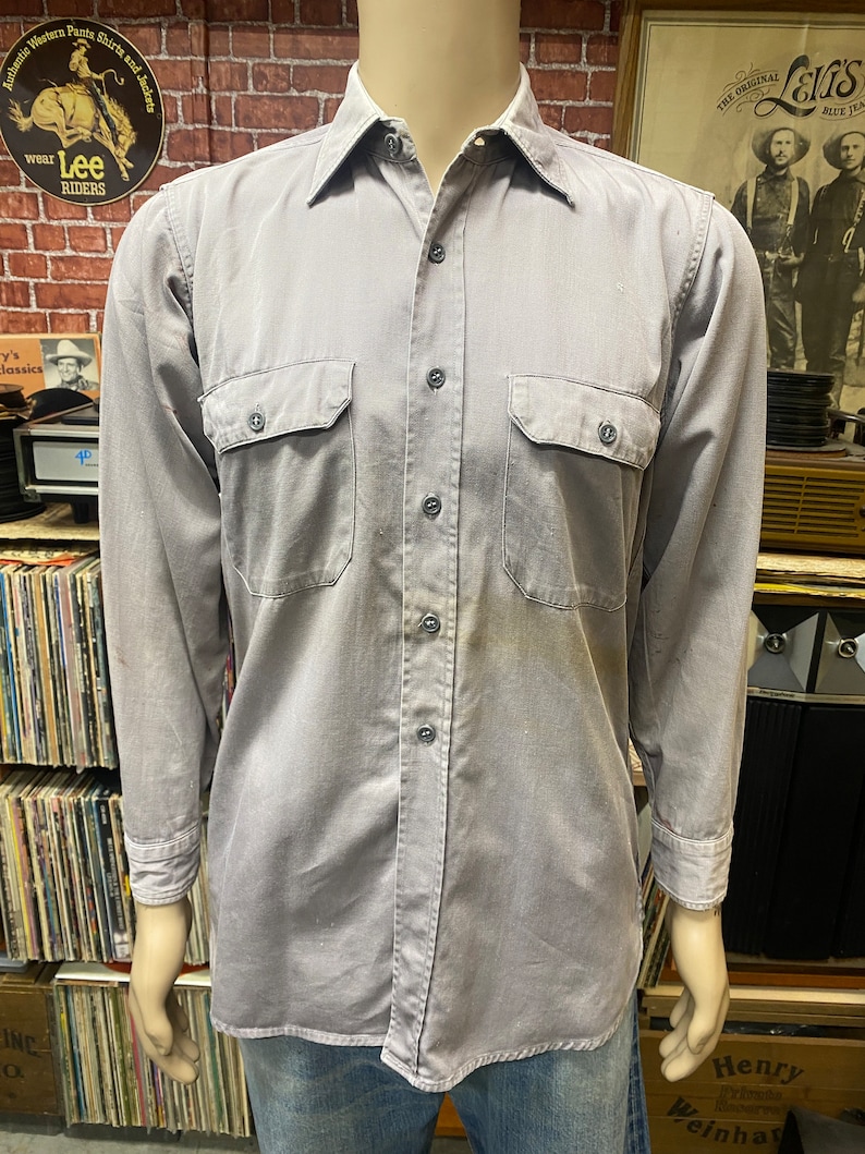 May include: A gray long-sleeved work shirt with two chest pockets and a button-down collar.