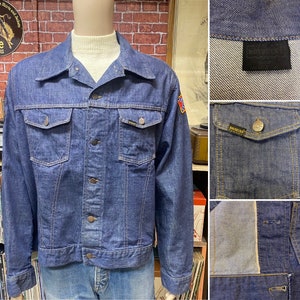 May include: A blue denim jacket with a Confederate flag patch on the right sleeve. The jacket has a button closure, two chest pockets, and two front pockets. The jacket is made by the brand "True-Spec".