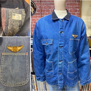 May include: A blue denim jacket with a corduroy collar and two patch pockets. The jacket has a  "Harley Davidson" logo patch on the left pocket and a smaller patch on the right pocket. The jacket has a button closure and is lined with a plaid fabric.