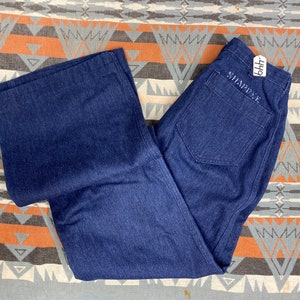 May include: A pair of dark blue denim jeans with a wide leg. The jeans have a label on the back pocket that says "Shaptee" and "BHT".