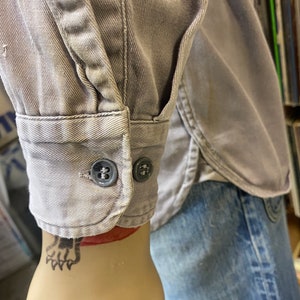 May include: A gray long-sleeved shirt with a button-up cuff. The shirt is made of a soft, textured fabric.