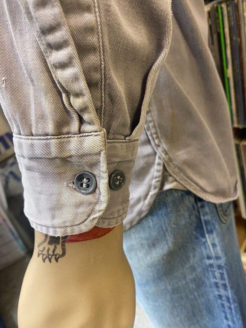 May include: A gray long-sleeved shirt with a button-up cuff. The shirt is made of a soft, textured fabric.
