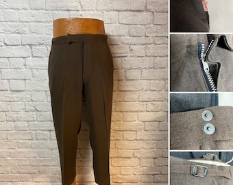 May include: Dark brown trousers featuring a metal zipper fly, a side tab adjuster with a buckle, and two circular metal buttons at the waist. A small red Levi's brand tag is visible on the side seam of the textured fabric.