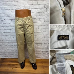 May include: Tan Levi's Sta-Prest pants. The pants are displayed on a mannequin and have a straight leg cut. The zipper and a label that reads "Levi's Sta-Prest One Crease Clothing" are visible. The pants are size 12.