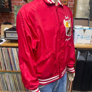 May include: Red satin baseball jacket with white and red striped trim. The jacket has a large embroidered patch on the left side with the text "Lank" and "Prelate".