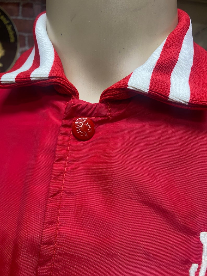 May include: Red satin baseball jacket with a white and red striped collar. The jacket has a single button closure.