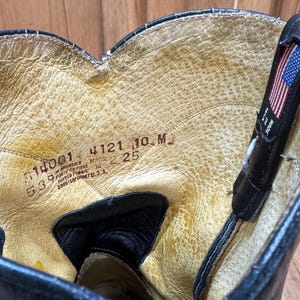 Op de afbeelding: Close-up van de binnenkant van een zwarte leren laars. De binnenkant van de laars is lichtbruin van kleur met zichtbare slijtage. De laars heeft een label met de tekst "MADE IN U.S.A." en andere nummers.