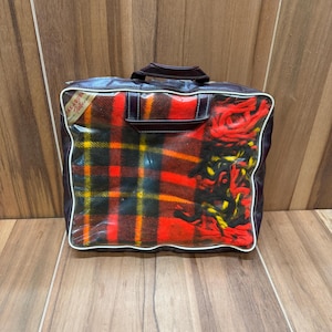 May include: A vintage plaid travel blanket in a brown leather carrying case with a clear plastic window. The blanket is red, black, yellow, and white.
