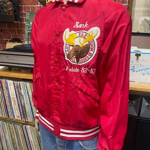 May include: Red satin varsity jacket with white and red striped trim. The jacket has a large embroidered patch with a moose and the text "PAP Loyal Order of Moose Prelate 82-83".