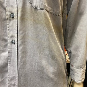 May include: A gray work shirt with a button-up front and a single chest pocket. The shirt has a faded appearance and is made of a durable fabric.