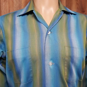 May include: A long-sleeved button-down shirt with a blue, green, and white ombre stripe pattern. The shirt has a collar and a pocket on the left side.