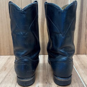 Op de afbeelding: Een paar zwarte leren cowboylaarzen. De laarzen hebben een klassiek ontwerp met een puntige neus en een gestapelde hak. De laarzen zijn ongeveer 25 cm hoog.