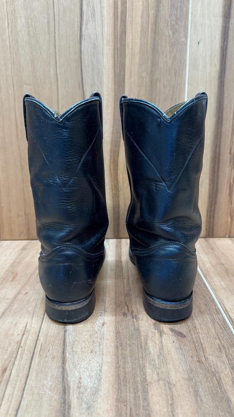 Op de afbeelding: Een paar zwarte leren cowboylaarzen. De laarzen hebben een klassiek ontwerp met een puntige neus en een gestapelde hak. De laarzen zijn ongeveer 25 cm hoog.