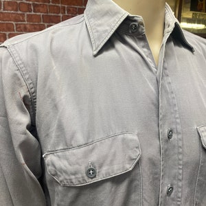 May include: A gray long-sleeved button-down shirt with a single chest pocket and a button closure.