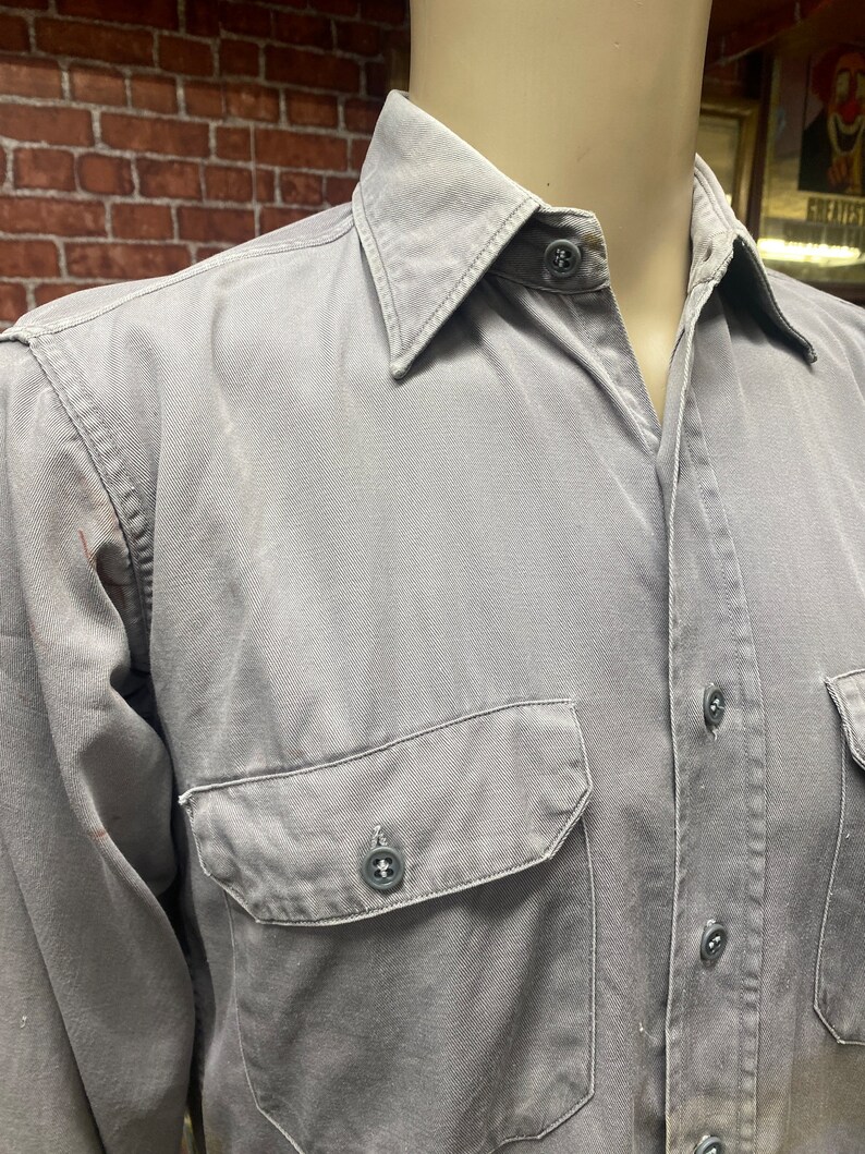 May include: A gray long-sleeved button-down shirt with a single chest pocket and a button closure.