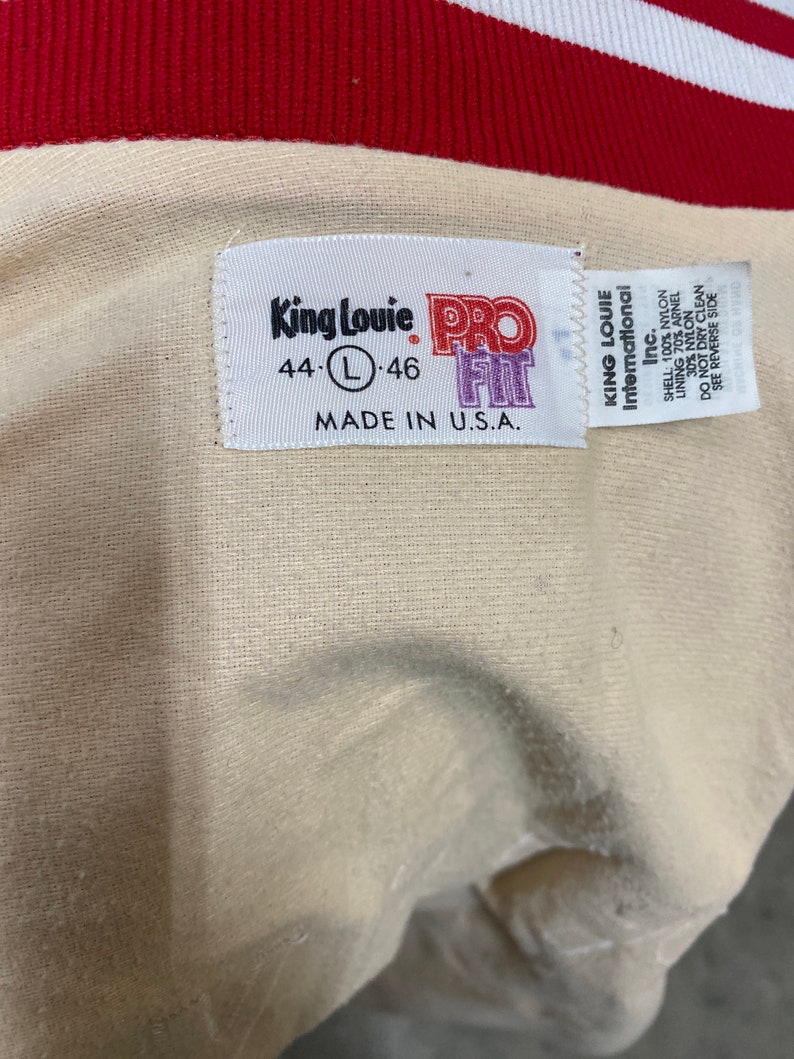 May include: A white tag with the text "King Louie International Inc." and "Pro Fit" in purple. The tag also includes the size "44-L-46" and the text "Made in U.S.A."