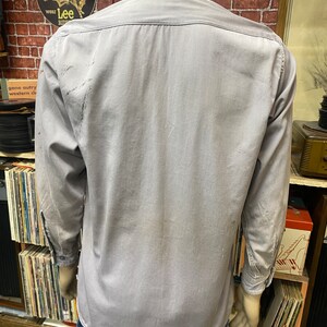 May include: A gray long-sleeved work shirt with a button-down collar. The shirt has a faded appearance and is slightly wrinkled.