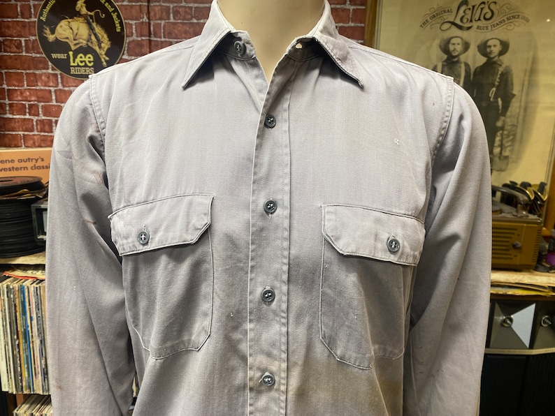 May include: A gray long-sleeved work shirt with two chest pockets and button closure.