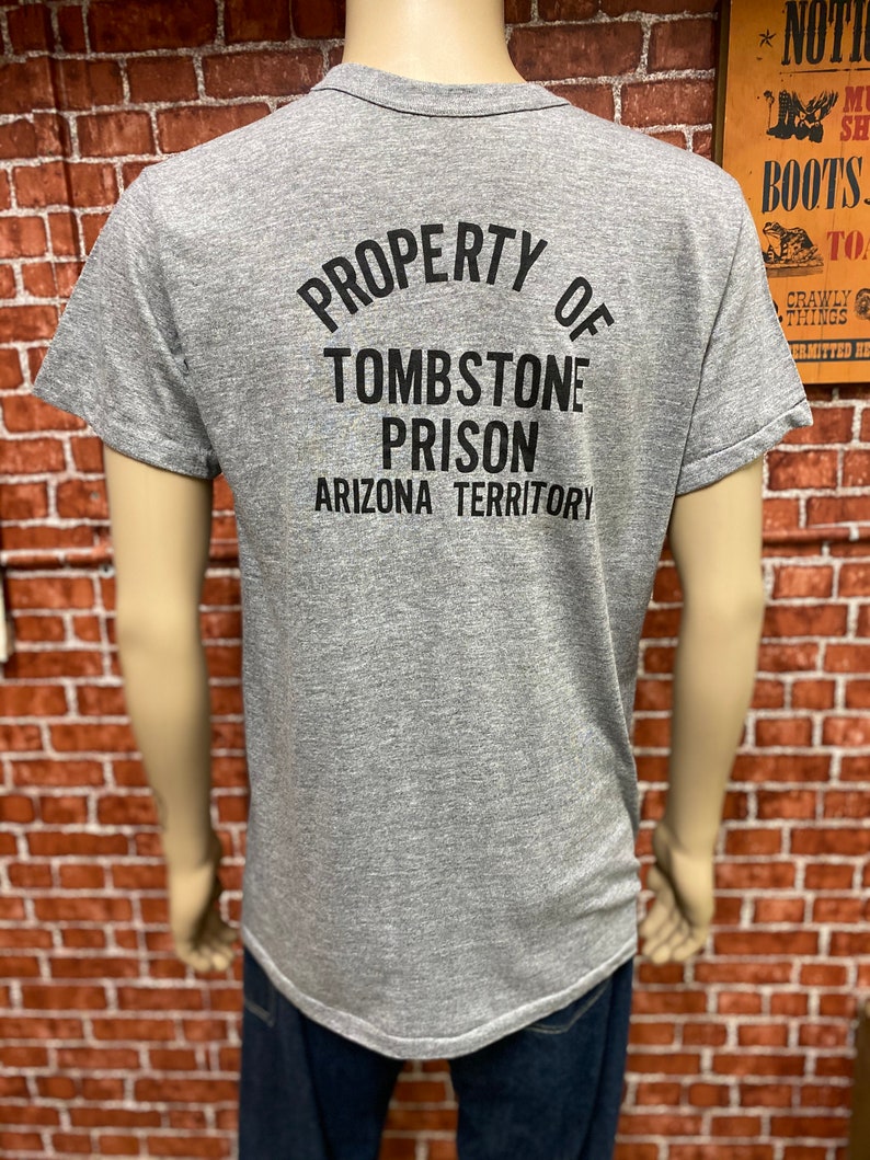 May include: Gray t-shirt with a black graphic that reads "PROPERTY OF TOMBSTONE PRISON ARIZONA TERRITORY".