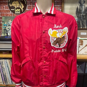 May include: Red satin bomber jacket with white and red striped trim. The jacket features an embroidered moose with the text "Loyal Order of Moose" and "Prelate 82-83".