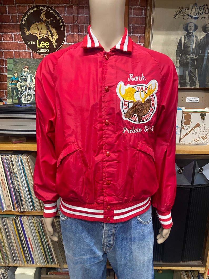 May include: Red satin bomber jacket with white and red striped trim. The jacket has a button closure and a large embroidered patch on the left chest featuring a moose and the text "Loyal Order of Moose" and "Pap Prelate 82-8".