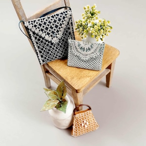 Puede incluir: Mini bolsos en blanco y negro, y un pequeño bolso marrón con asa marrón. Los bolsos están sobre una pequeña silla de madera con un jarrón blanco con flores y un jarrón blanco con hojas verdes.