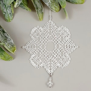Peut inclure: Ornement de flocon de neige en crochet blanc avec une goutte de perle de cristal. Le flocon de neige est complexe et délicat, avec une bordure perlée.