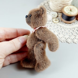 May include: A small brown teddy bear with a red and white lace collar. The bear is standing on its hind legs and is looking to the left.