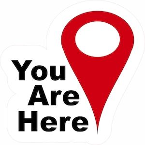May include: A white sticker with a red location pin graphic and the words "You Are Here" in bold black font. The pin is a classic teardrop shape, indicating a specific spot.