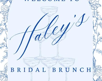 以下が含まれることがあります： 装飾的なフォントで「WELCOME TO Haley's BRIDAL BRUNCH」と書かれた水色の看板。シャンパングラスのスタックと、青と白の花柄のボーダーが特徴です。