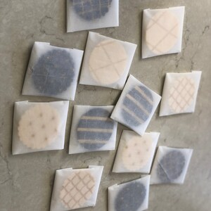 以下が含まれることがあります： 白い羊皮紙に包まれた丸いクッキーが12個あります。クッキーには、黒と白のストライプ、黒と白の市松模様、ベージュと茶色の市松模様など、さまざまなパターンがあります。